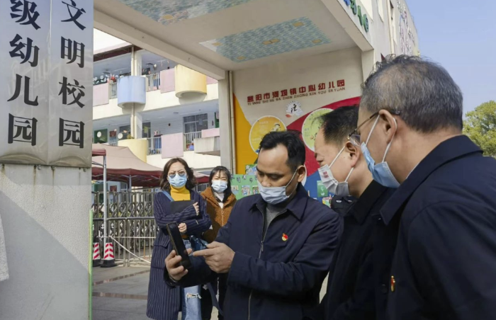 圖為樂運成（右二）通過手機客戶端查看大通湖區第一實驗幼兒園廚房實時視頻。